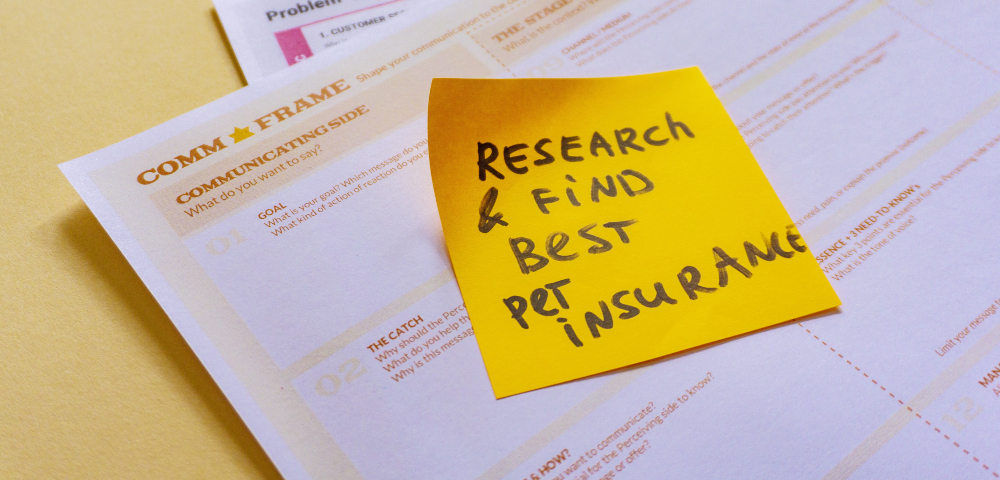 Papers on desk with white post-it note that says, "Research & Find Best Pet Insurance". Liam Hennessy, Digital Strategist